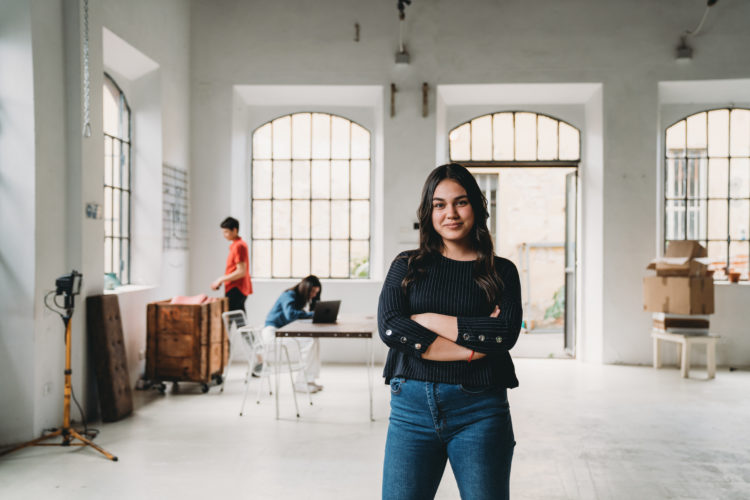 Portrait of a young woman in a modern loft. Other people in the background. Mixed race ethnicity.