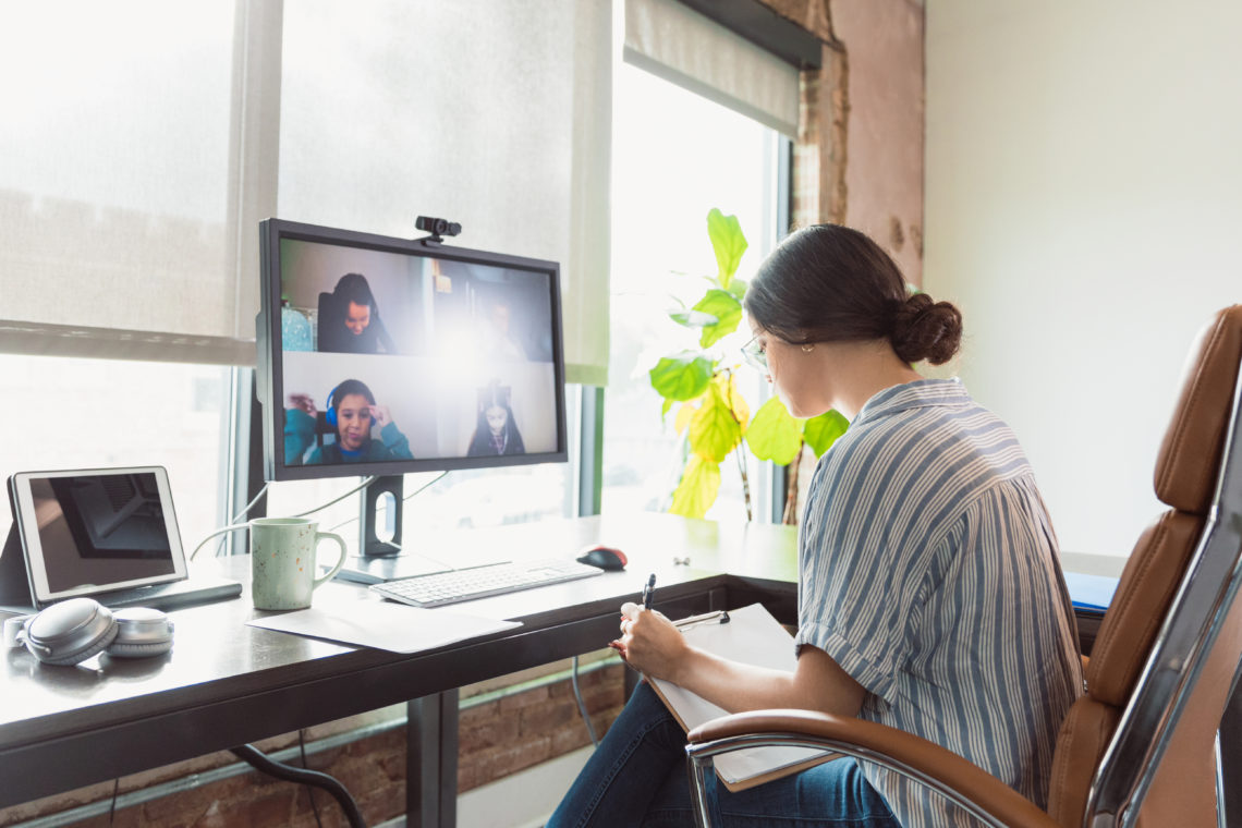 During the COVID-19 pandemic, a young adult female teacher takes notes as she talks with a group of elementary students during an online teaching s...